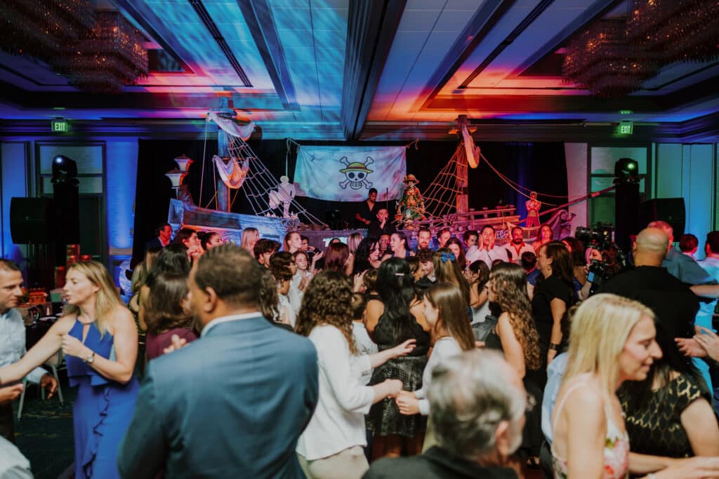 Guests dancing at a One Piece-themed Bar Mitzvah with pirate ship décor and colorful ballroom lighting.